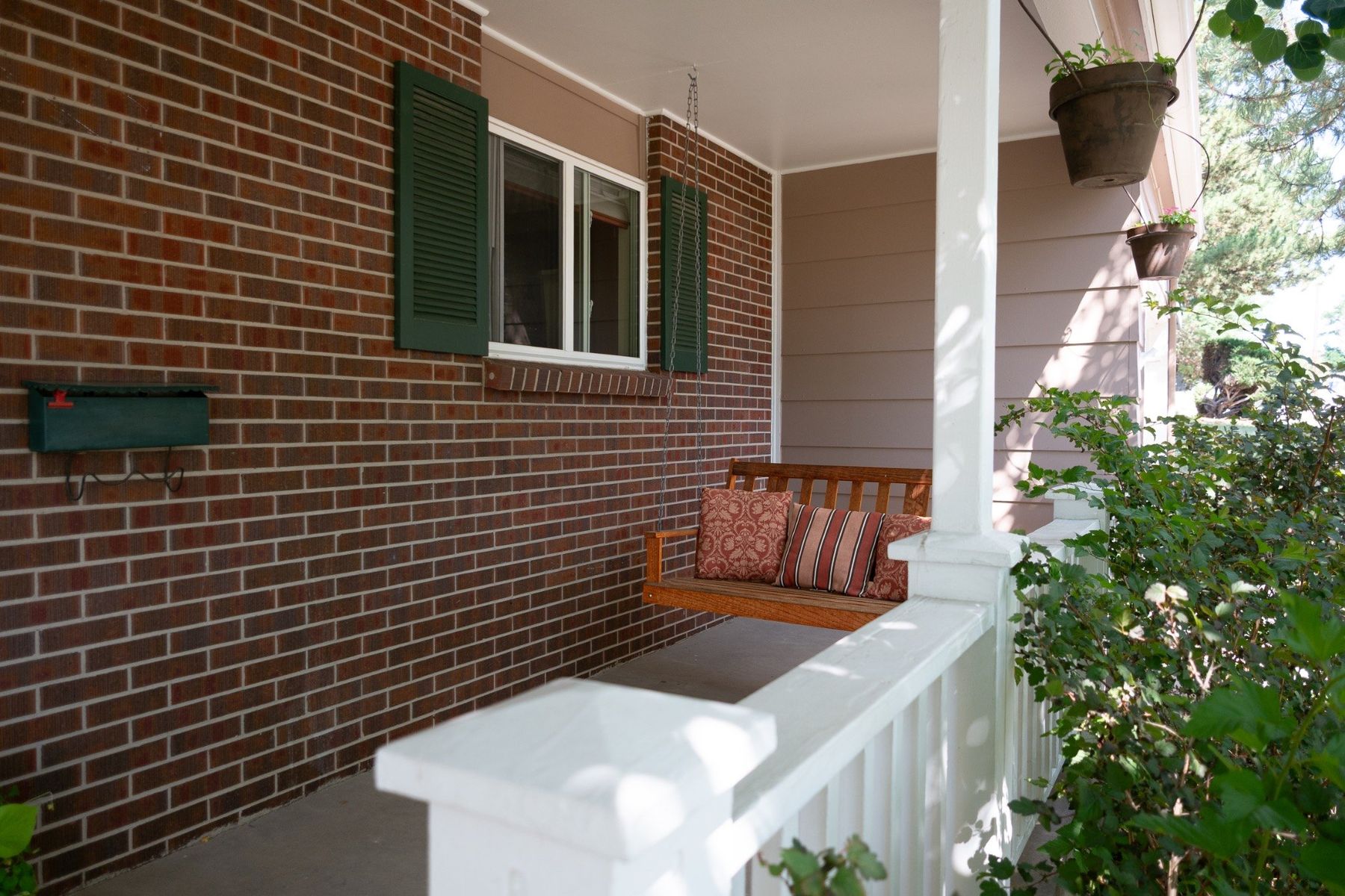 Brick front porch with hanging bench and greenery
